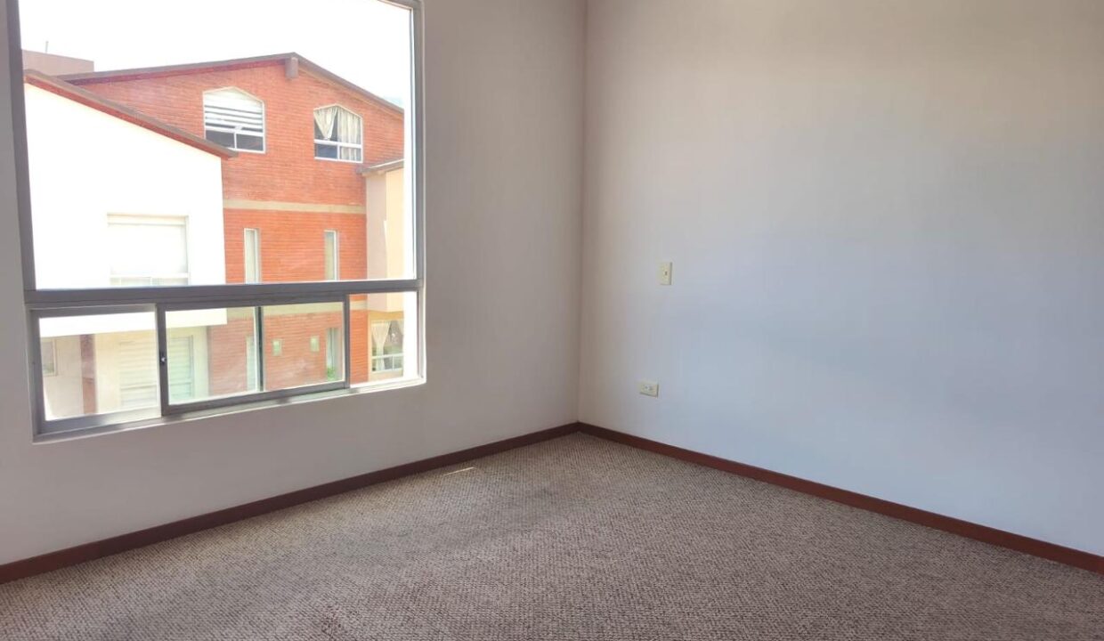 Dormitorio amplio con ventanal y alfombra en casa en venta en Pomasqui, Quito