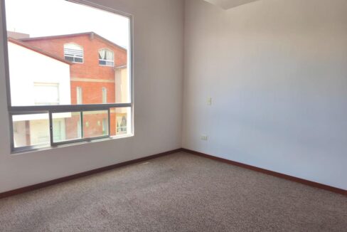 Dormitorio amplio con ventanal y alfombra en casa en venta en Pomasqui, Quito