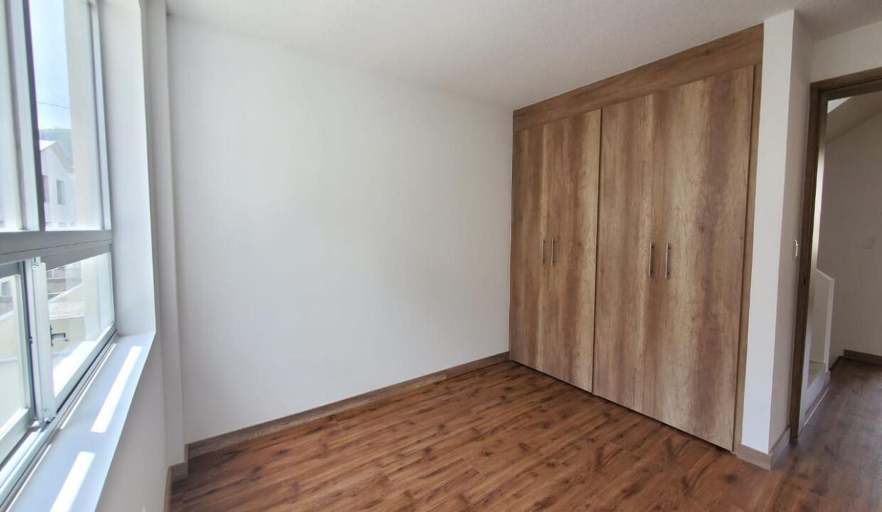 Dormitorio con closet de madera y piso flotante en casa en venta en Pomasqui, Quito