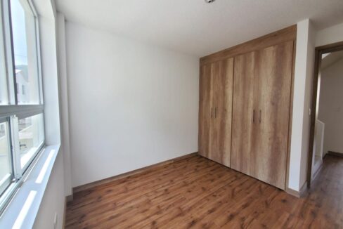 Dormitorio con closet de madera y piso flotante en casa en venta en Pomasqui, Quito